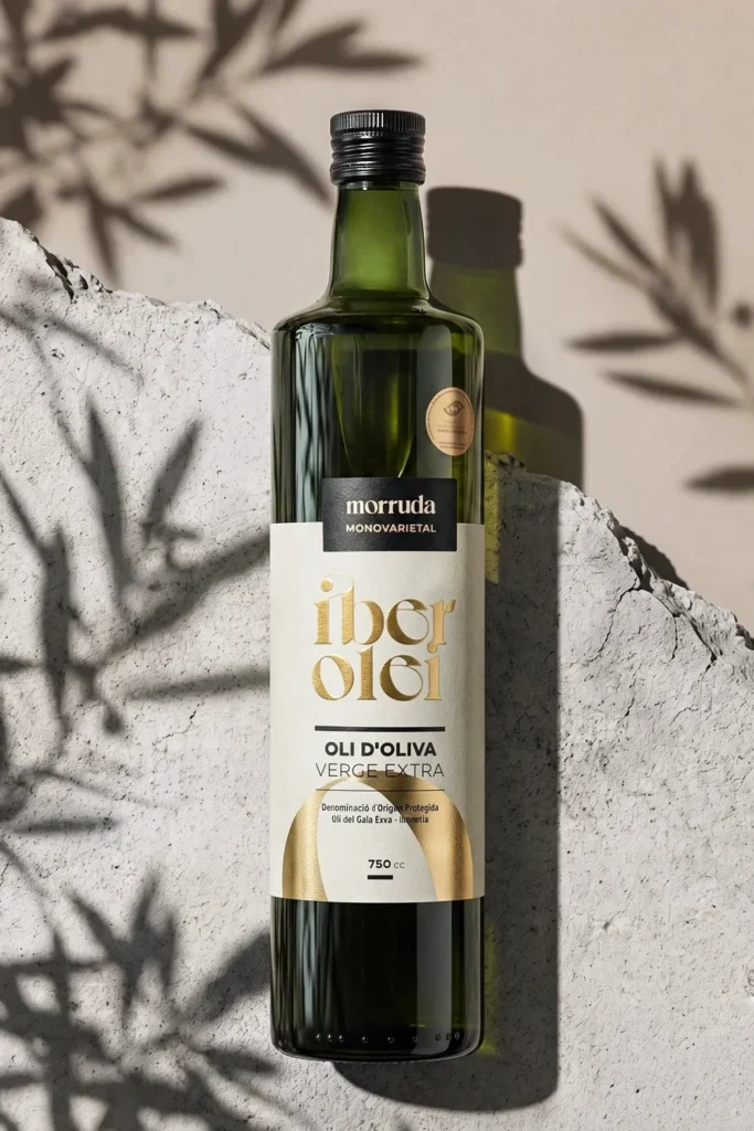 Fotografia professiona d'oli d'oliva verge extra ampolla vidre verd composició artística ombres fulles olivera fons pedra Catalunya